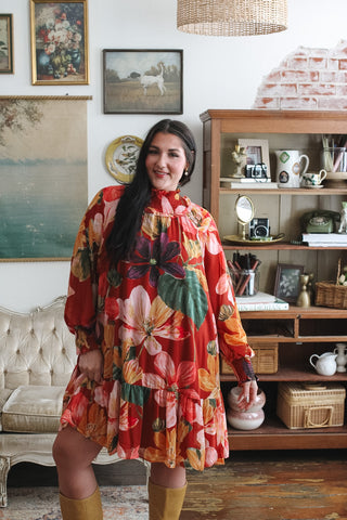 Woman wearing a vibrant floral long-sleeve mini dress in a cozy, vintage-style room.