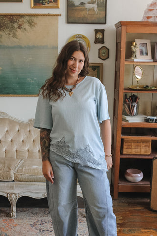 Woman wearing a light blue top and pants in a room with a couch and bookshelf.