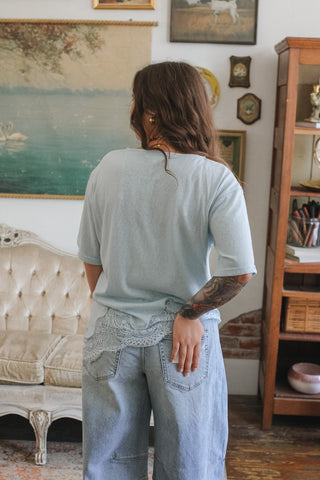 Person wearing a light blue t-shirt and jeans standing in a room with vintage decor.