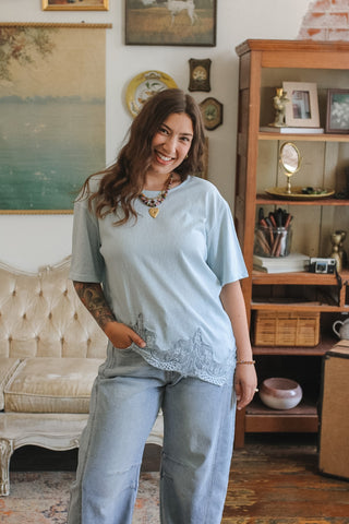 Woman wearing a light blue outfit standing in a room with a couch and decorative items.