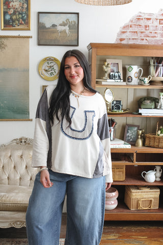 Woman wearing beige patchwork long sleeve top with horseshoe applique