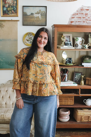 Woman wearing golden yellow floral top with scalloped ruffle trim