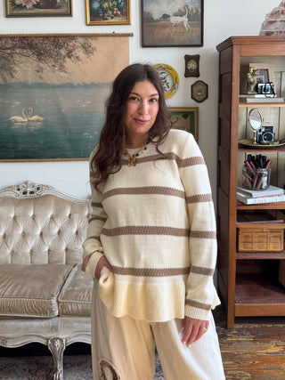 Woman wearing the Della striped knit pullover sweater in cream with taupe stripes and a ribbed hem, styled with cream pants