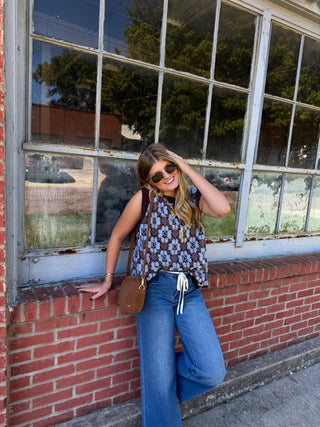 Woman wearing the Maren floral knit sweater vest in chocolate brown with textured baby blue flowers, styled with wide leg jeans
