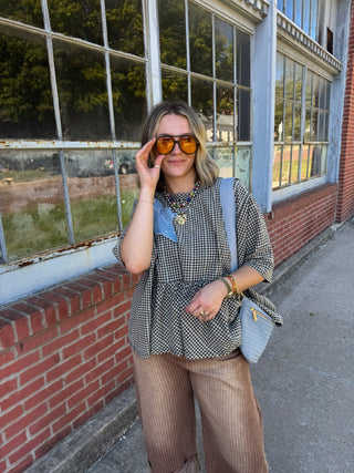 Woman wearing the Briar black and white gingham patchwork ruffle top with a denim star patch, styled with brown striped pants and a light blue crossbody bag