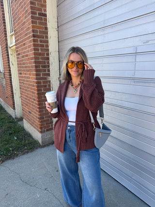 Woman wearing the Miller chunky knit tie cardigan in warm brown with a tassel belt, styled with a white tank and wide leg jeans