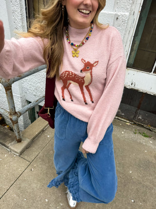 Woman wearing the Bambi blush mock neck sweater with a knit fawn icon and balloon sleeves with blue corduroy wide leg pants