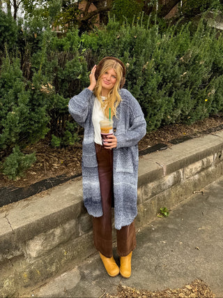 Woman wearing the Teddy navy long hooded knit cardigan with a marled ombre finish and patch pockets over a white tee and brown wide leg pants