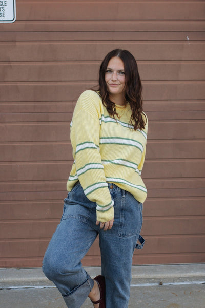 Woman wearing a yellow striped sweater and blue jeans standing in front of a brown garage door.