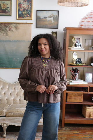 Woman wearing the Lena mineral washed babydoll blouse in washed brown with a ruffled mock neck, pintucked yoke and puffed long sleeves