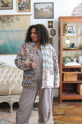 Woman wearing the Goldie mauve mixed medium quilted jacket with embroidered florals, a woven border print and lace pockets over striped overalls