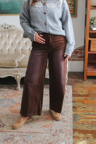 Woman wearing the Collins brown vintage washed corduroy wide leg pants with a gray snowflake knit cardigan and tan suede loafers