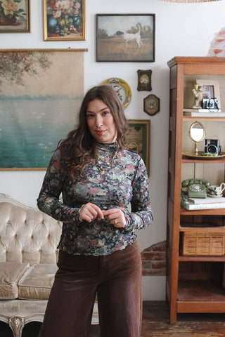 Woman wearing the Billie black floral velvet burnout mock neck top with long sleeves and brown corduroy pants