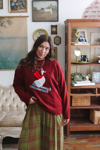 Woman wearing the Mabel red crewneck sweater with a skiing duck graphic and green plaid wide leg pants