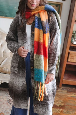 Woman wearing a colorful brushed plaid fringe scarf in orange, blue, olive and turquoise over a chocolate brown cardigan