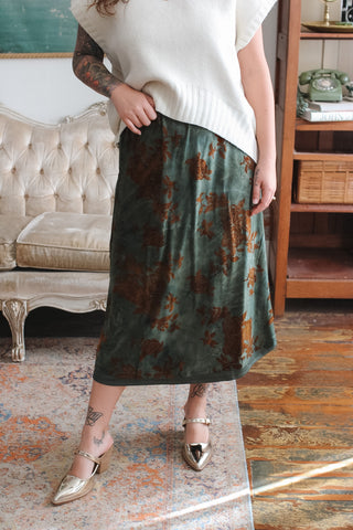 Woman wearing the Shiloh dark teal floral velvet burnout midi skirt with rust roses and gold pointed mules