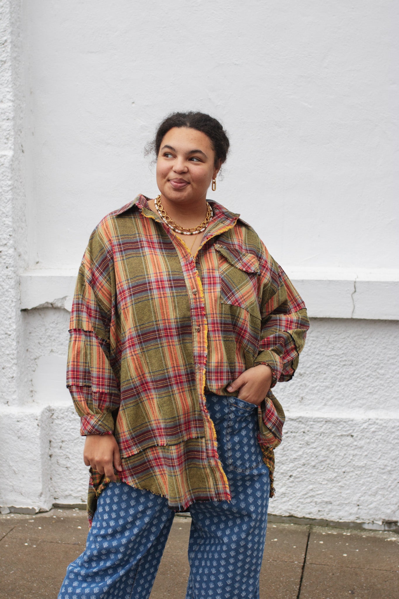 Person wearing a plaid shirt and blue patterned pants standing against a white wall.