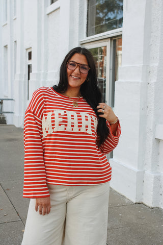 Woman wearing a red and cream striped oversized top with an off white MERRY applique and cream wide leg pants