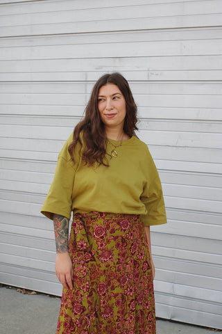 Woman wearing an olive green oversized cotton tee with wide sleeves over a red and olive floral wrap skirt