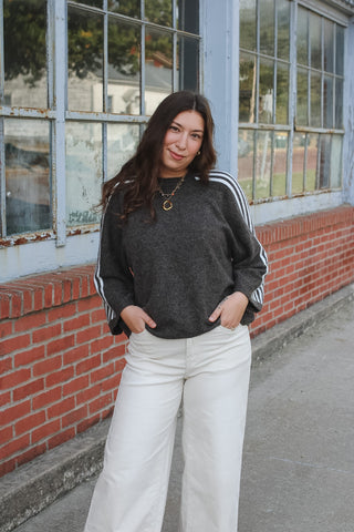 Woman wearing a washed brown knit sweater with three cream stripes down the sleeves and cream wide leg pants