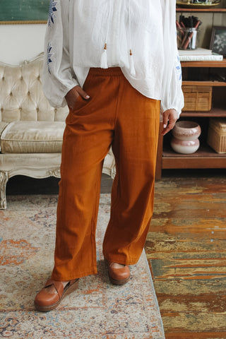 A person wearing loose-fitting rust-colored wide-leg pants paired with a white embroidered blouse.