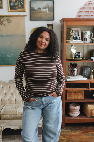 Woman wearing a brown and white striped long-sleeve sweater with relaxed-fit blue jeans in a cozy room.