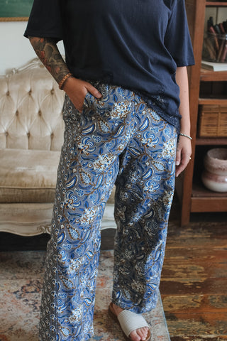 A person wearing loose blue paisley print pants with a dark navy t-shirt, standing in a living room setting.