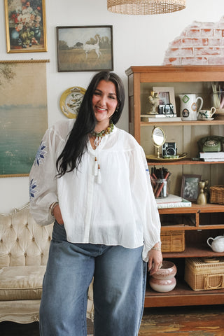 Woman wearing a white blouse with blue quilted embroidery on sleeves, paired with wide-leg jeans.