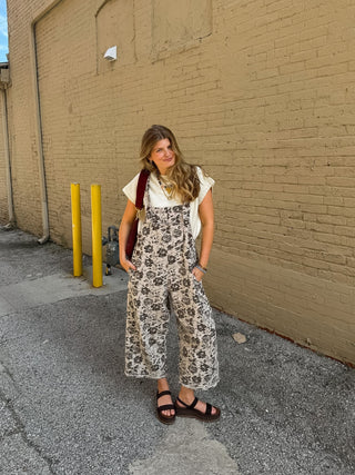 Woman wearing ivory floral denim overalls with adjustable straps