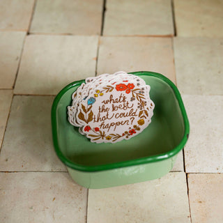 A round white sticker with a floral border and the handwritten text 'what's the best that could happen?